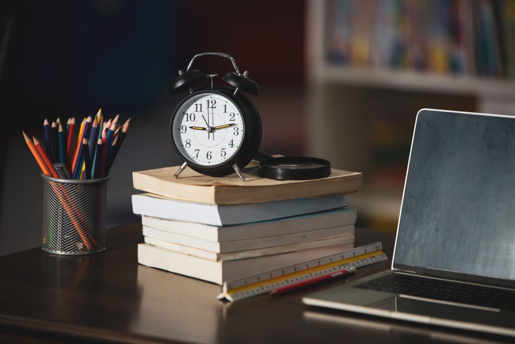Book,laptop,pencil,clock on wooden table in a library