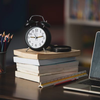 Book,laptop,pencil,clock on wooden table in a library